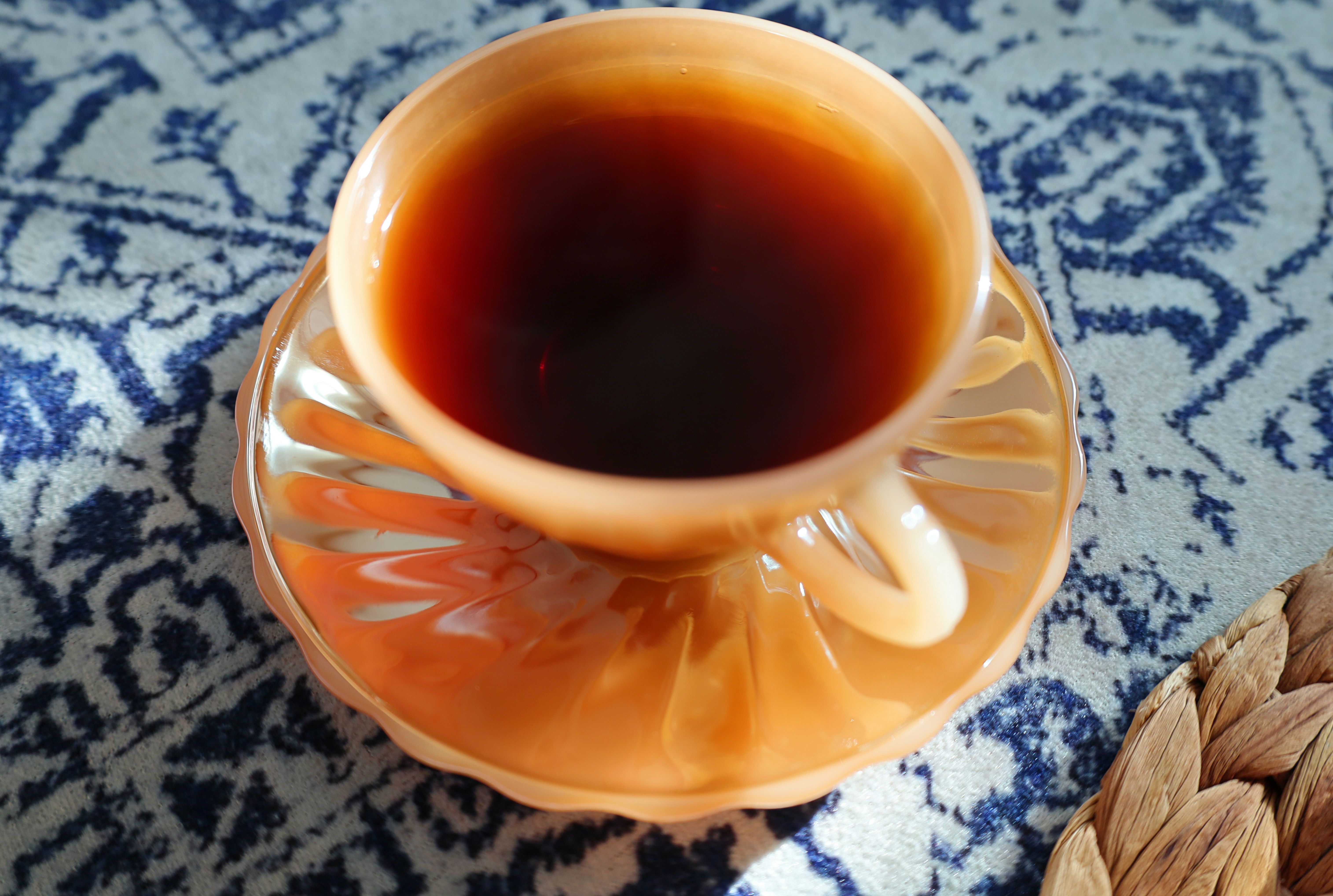 Top view of black tea served in a vintage amber glass cup on a patterned tablecloth.