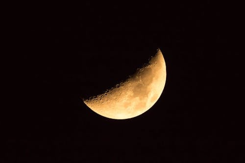 Yellow half moon with spots hiding in darkness of endless universe sky on black background