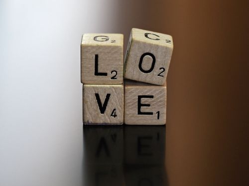Free Wooden letter dice spelling LOVE with reflections on a shiny surface, conveying an intimate and thoughtful theme. Stock Photo