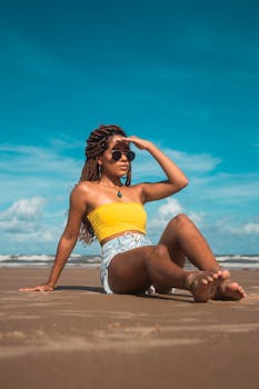 Full body slim woman with dreadlocks chilling on coast and looking away in sunshine