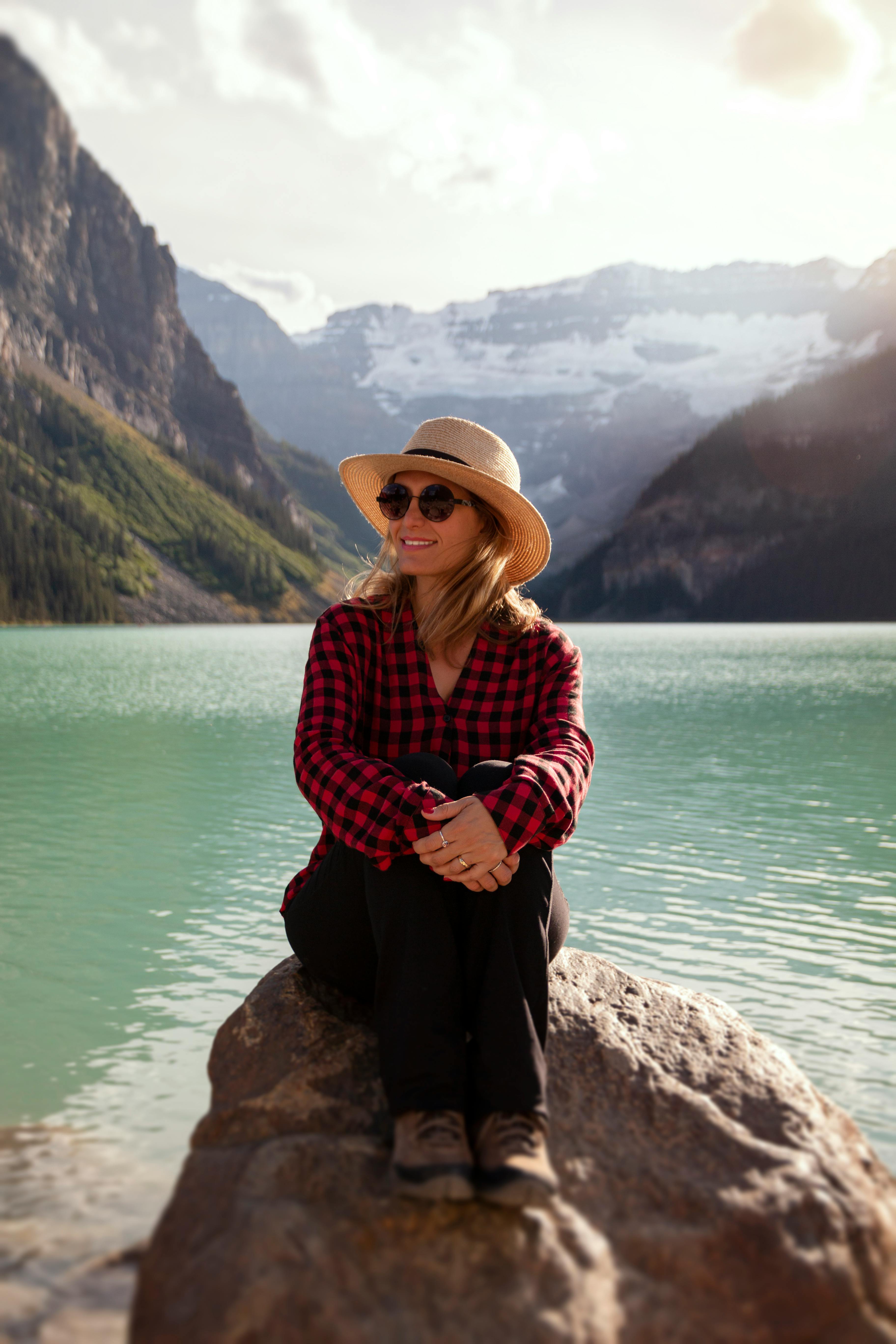 Woman in plaid shirt and hat enjoys the view at Lake Louise, Alberta, with mountains and turquoise waters.