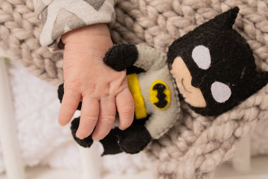 Close-up of a baby holding a Batman plush toy, evoking warmth and innocence.