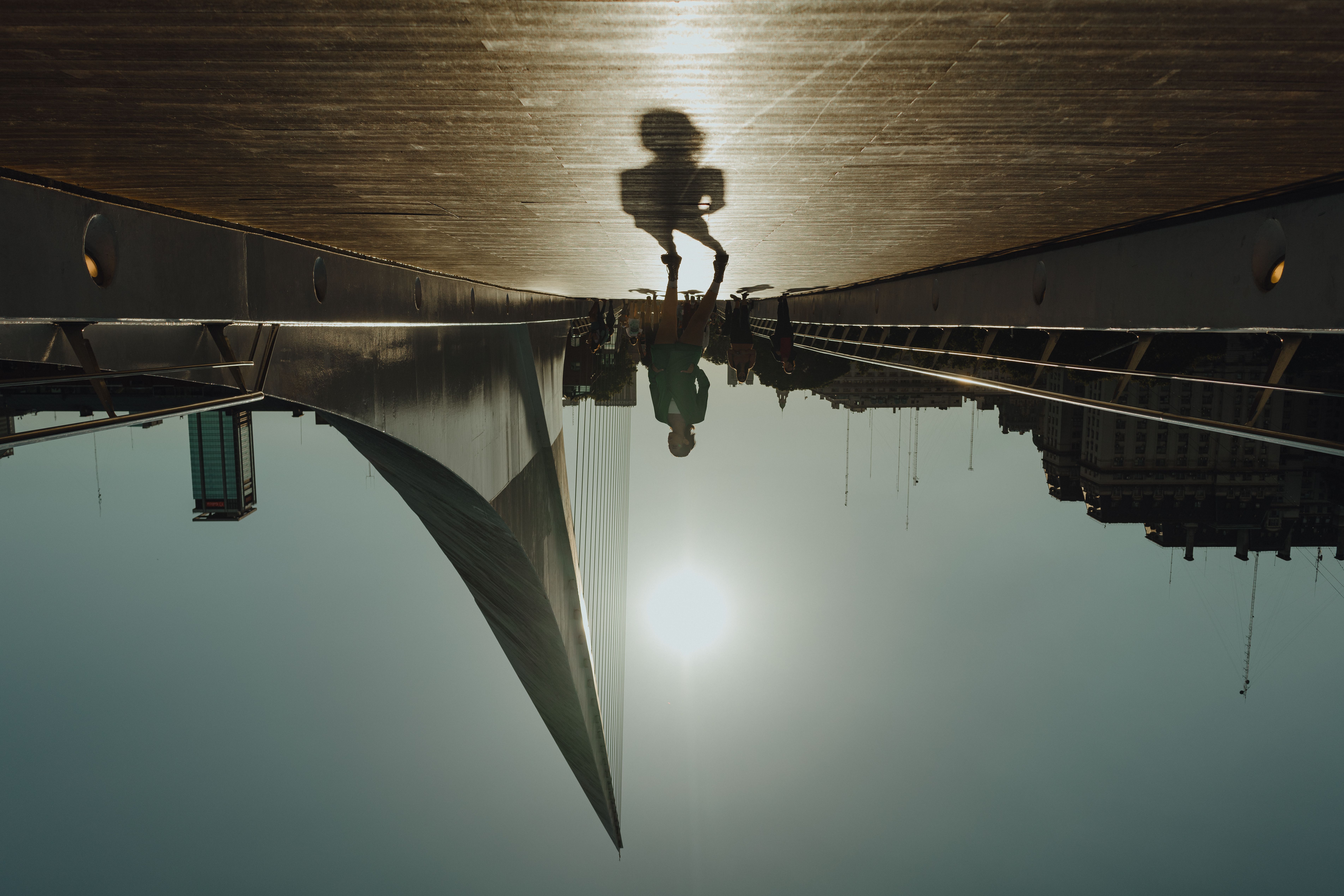 Artistic silhouette of a person walking on a modern bridge against the sun.