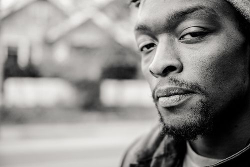 Free Black and white of crop suspicious young unshaven African American male in casual wear looking at camera while standing near road and houses in town Stock Photo