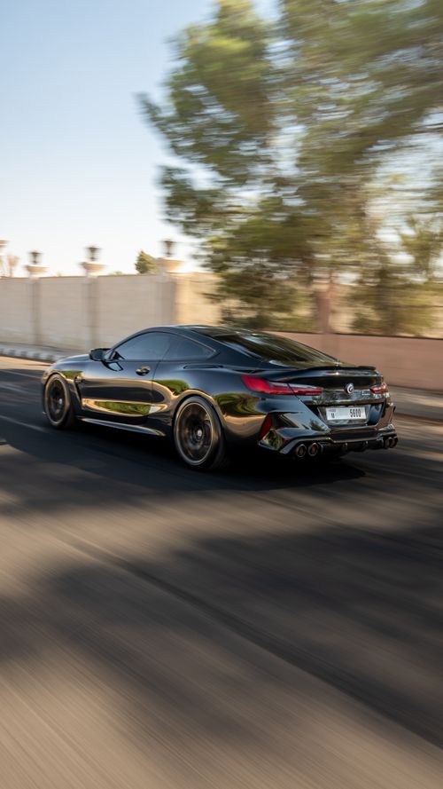 Free Dynamic shot of a sleek black car racing down a sunlit road, exuding speed and elegance. Stock Photo