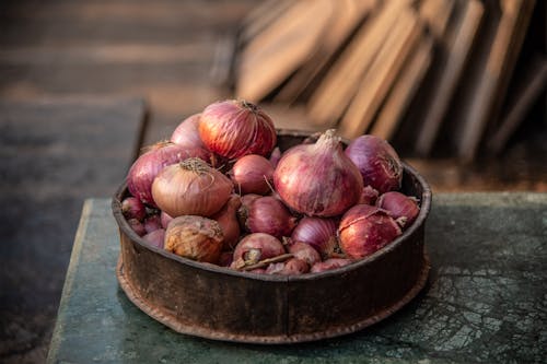 Old bowl with pile of red onions on rustic table