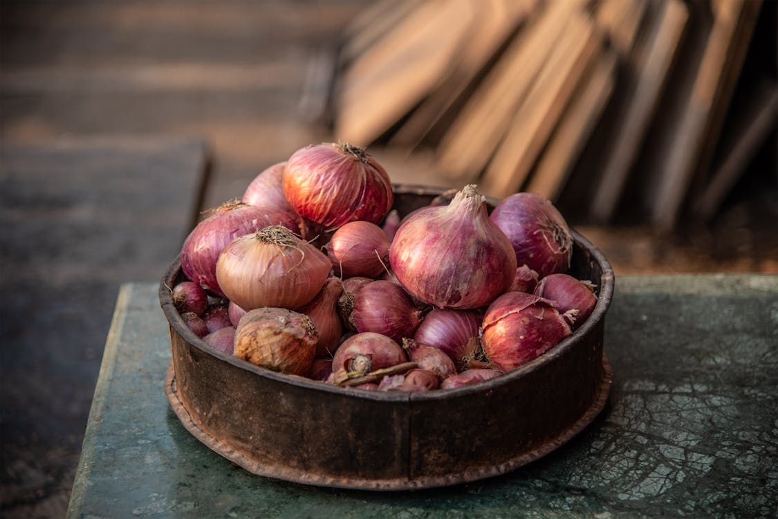 Old bowl with pile of red onions on rustic table