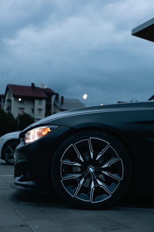 Free Black BMW M4 parked in an urban area at dusk, showcasing its sleek design and modern features. Stock Photo