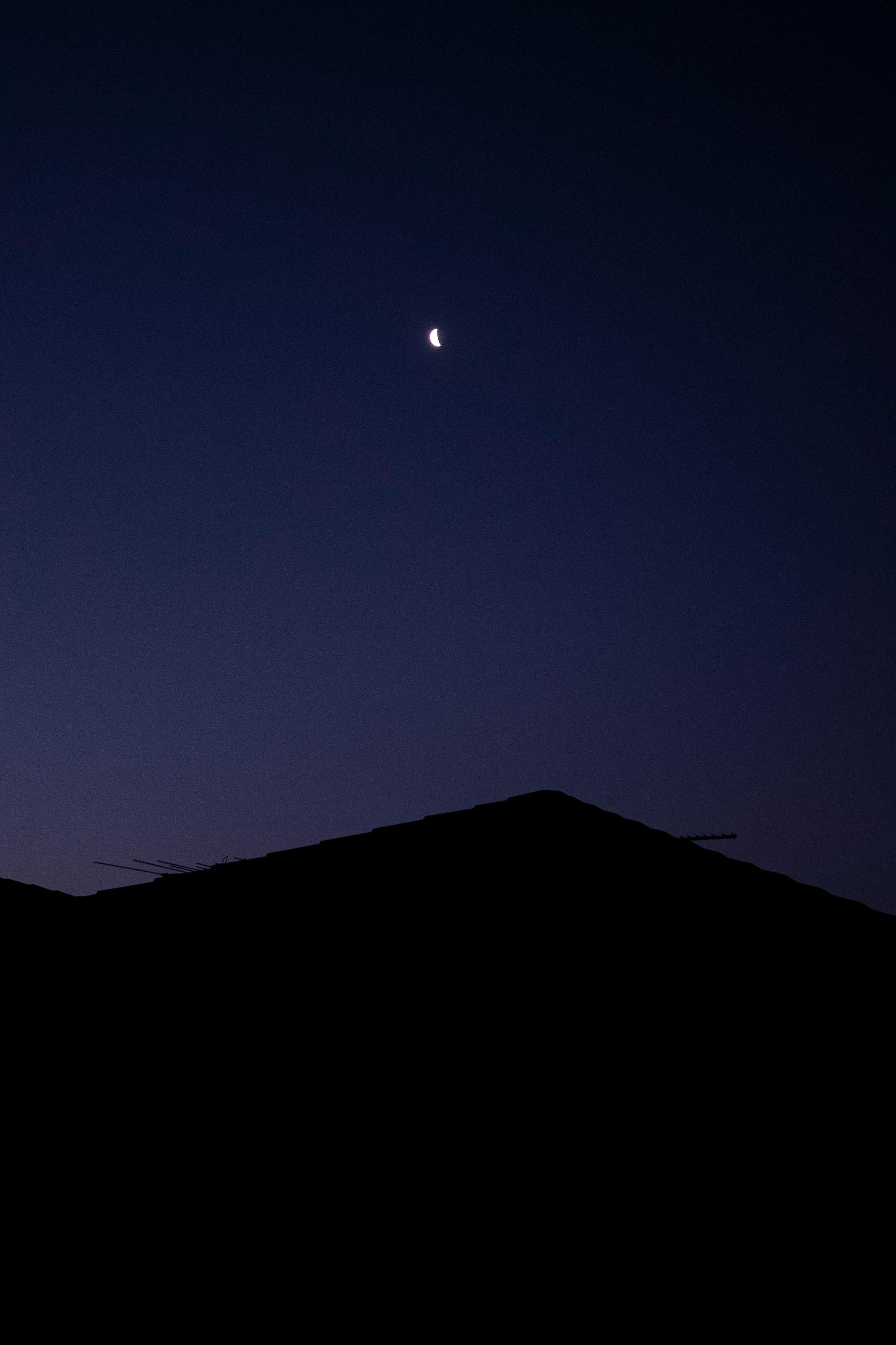 Minimalist silhouette of a roof with a crescent moon in the clear night sky above Melbourne, Australia.
