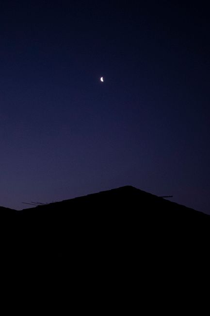 Minimalist silhouette of a roof with a crescent moon in the clear night sky above Melbourne, Australia.