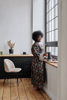 A woman in a cozy robe enjoys her morning coffee by the window, embracing a serene start to the day.
