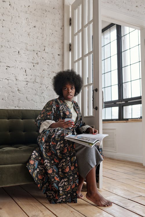 Free woman Sitting on a Sofa With a Magazine and a Smartphone Stock Photo