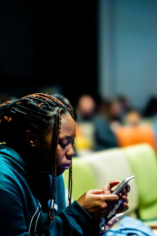 Free A young woman attentively uses her smartphone while seated indoors, surrounded by blurred background. Stock Photo