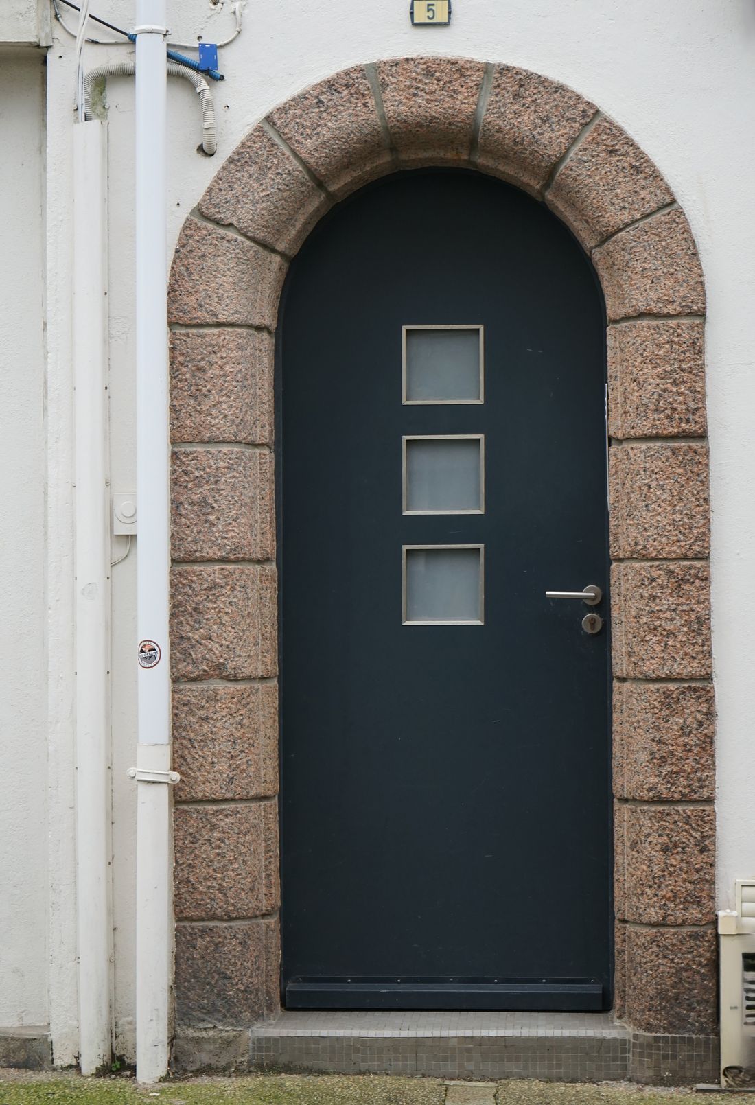 Porte d'entrée moderne anthracite sous une arche en pierre