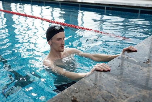 Free Active young man training in an indoor swimming pool, holding onto a pool edge. Stock Photo