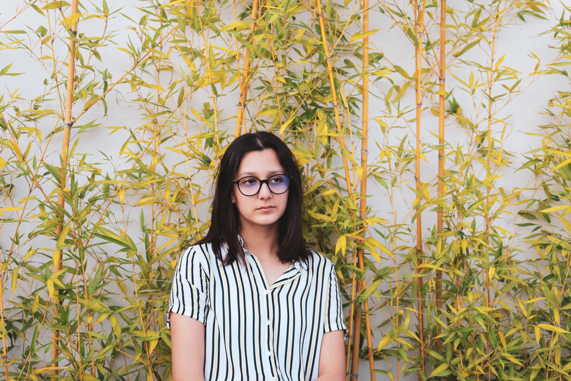 Teenage girl with glasses in striped shirt posing by bamboo plants in Guadalajara.