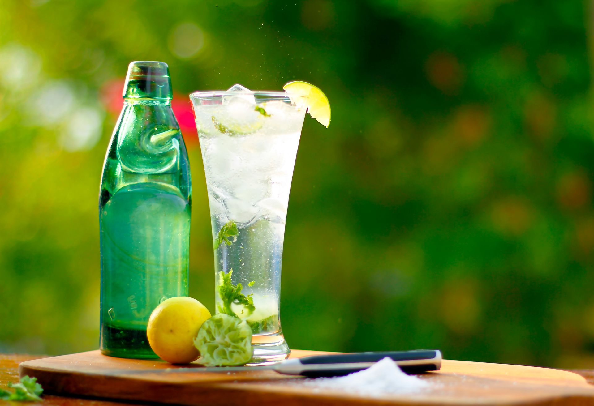 A tall glass of lime soda with ice and citrus fruits on a sunny day.