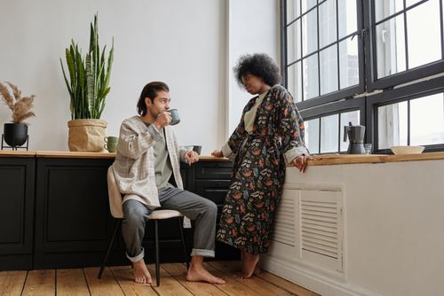 Free A relaxed morning scene with a couple enjoying coffee by a large window indoors. Stock Photo
