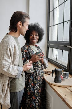 Happy couple enjoying morning coffee by the window in cozy robes.