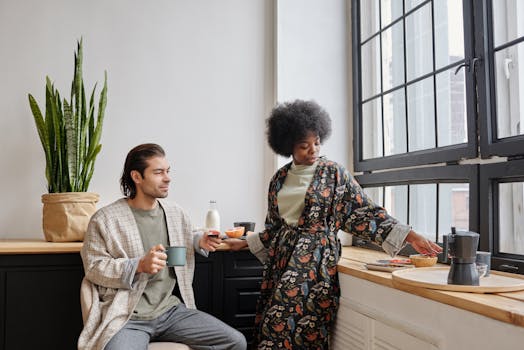 A couple enjoys morning coffee together by a large window, capturing a peaceful everyday life moment.
