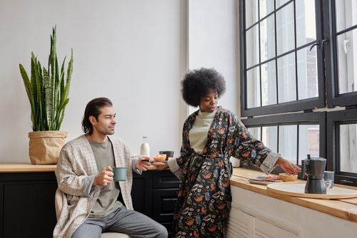 Free A couple enjoys morning coffee together by a large window, capturing a peaceful everyday life moment. Stock Photo