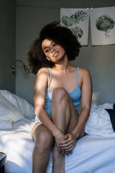 Woman enjoying a peaceful morning in a cozy bedroom, surrounded by soft linens and natural light.
