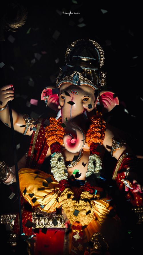 Free Colorful Ganesh idol adorned with flower garlands amidst celebratory confetti. Stock Photo