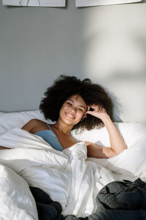 Free Smiling woman with curly hair relaxes in bed during a sunny morning. Stock Photo