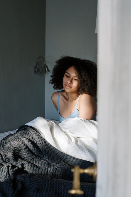 Free Young woman with curly hair relaxing in bed during the morning light. Stock Photo