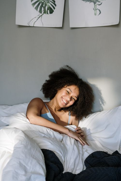 Free Smiling woman with curly afro hair enjoying a cozy morning in bed. Stock Photo