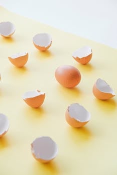 A still life of eggshells and a whole egg on a yellow surface with minimalistic composition.