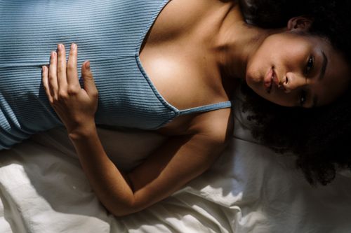 Free Woman enjoying a peaceful morning at home, lying in bed with soft sunlight. Stock Photo