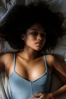 Beautiful woman with curly hair resting in bed, enjoying morning light.