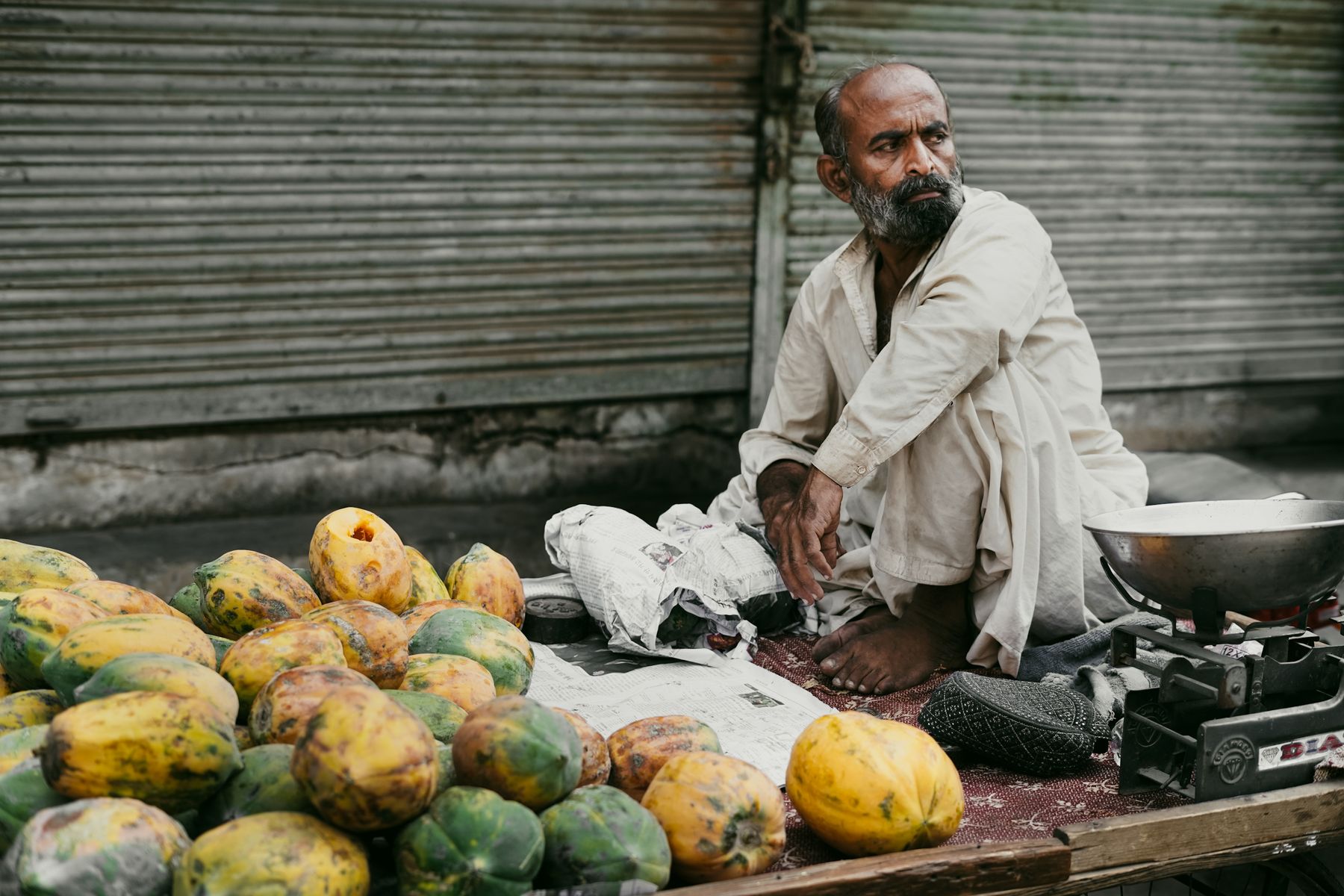 Street vendor sits beside his fresh papayas in Hyderabad, Sindh, showcasing local market culture.