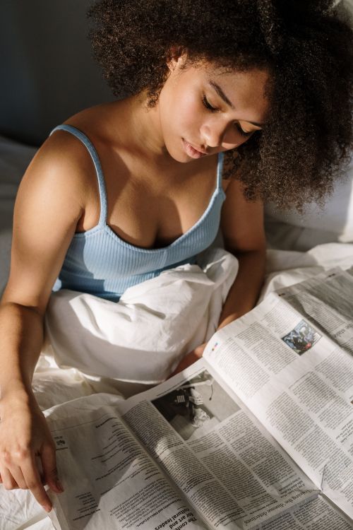 Free Woman in blue top reading newspapers in bed with morning sunlight. Stock Photo