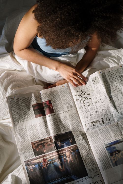 Free A woman enjoys a peaceful morning reading the newspaper in bed. Stock Photo