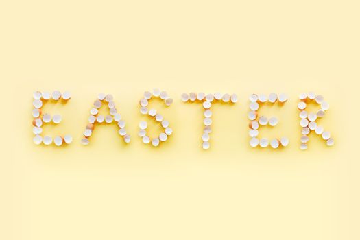 Artistic arrangement of empty eggshells spelling 'Easter' on a pale yellow backdrop.