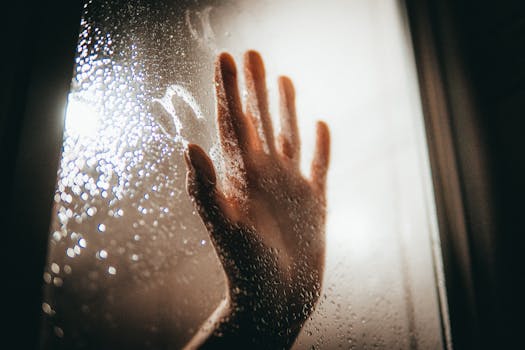 A dramatic photo of a hand pressed against a rainy window, evoking emotions of isolation and introspection.