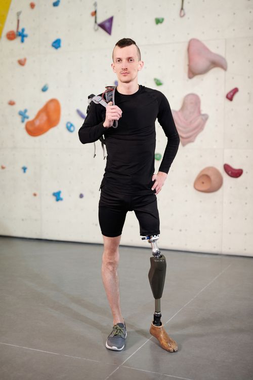 Free Young man with prosthetic leg confidently posing at indoor climbing gym, showcasing determination and strength. Stock Photo