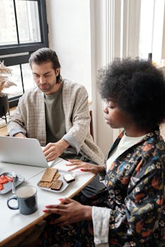 A couple works from home, sharing breakfast at a table with laptops.