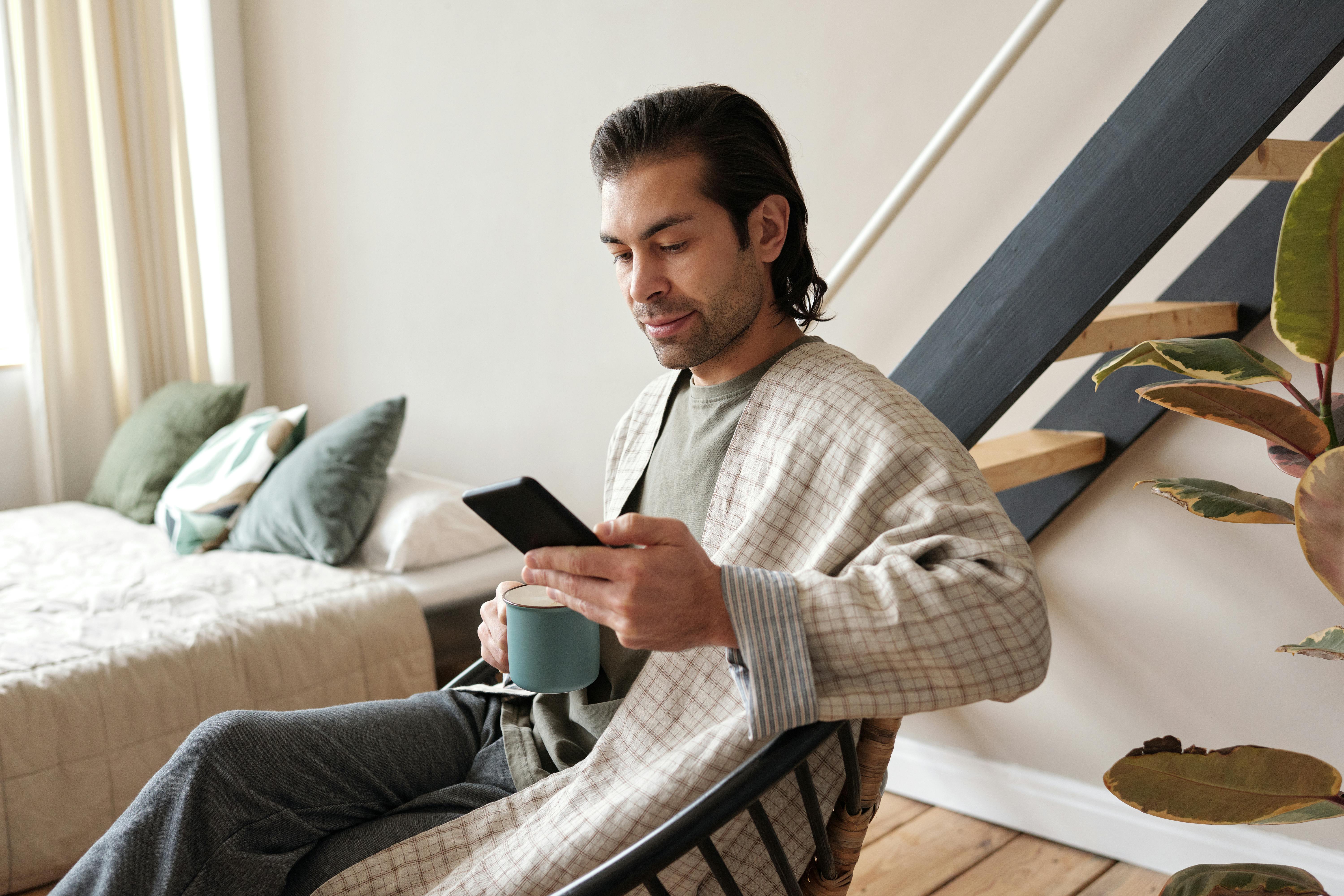 man looking at his cellphone while having coffee