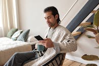 一名成年男子在室内喝着咖啡，用智能手机享受放松时光