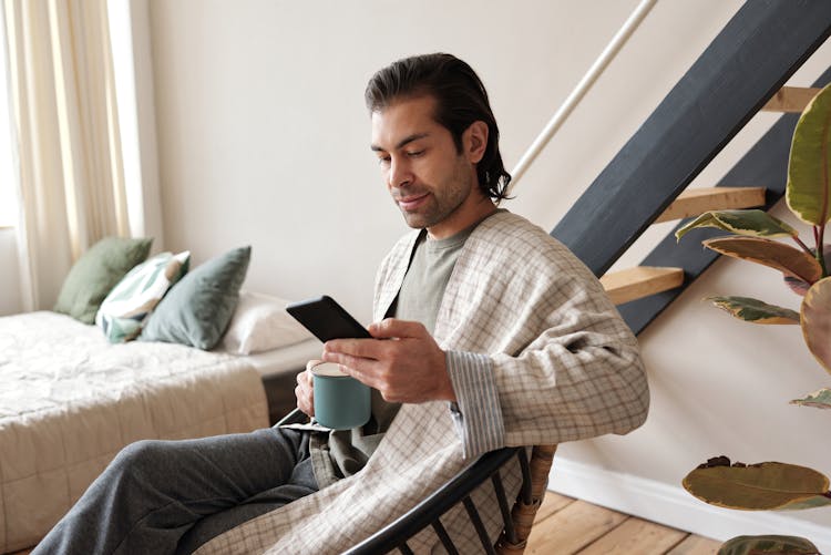 Man Looking At His Cellphone While Having Coffee