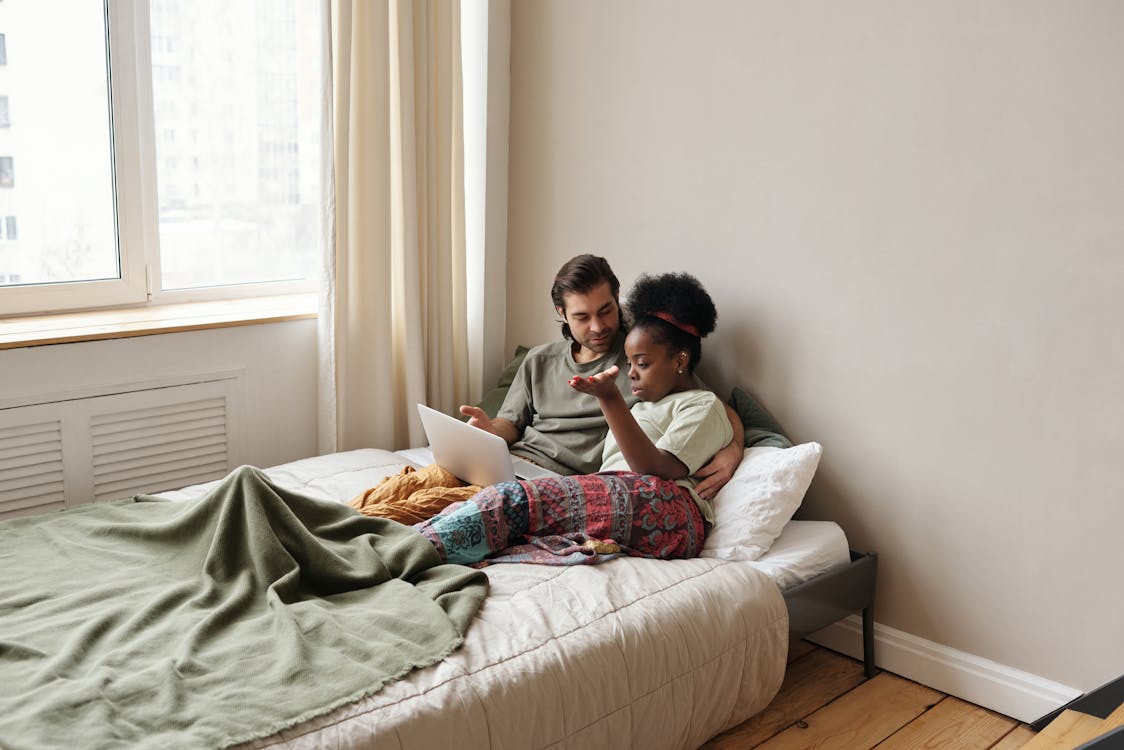 Couple Relaxing In Bed While Using Laptop