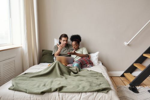 Free Multiracial couple watching content and relaxing on bed, sharing moments together. Stock Photo