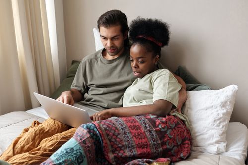 Free A couple enjoying leisure time together on a bed using a laptop, signifying modern relaxation. Stock Photo