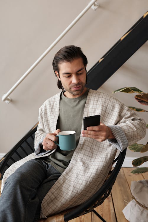 Man Sitting With a Mug and a Smartphone