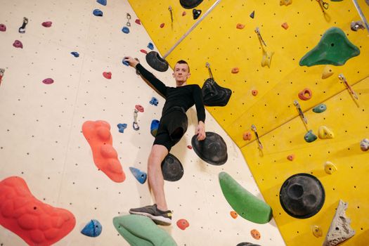 A determined male climber scaling a colorful indoor climbing wall. Featuring a leg prosthesis, he embodies strength and challenge.