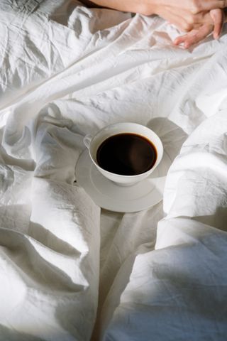 A cup of black coffee resting on rumpled white bedding, photo by cottonbro studio on Pexels