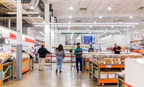 Customers shopping in a busy wholesale warehouse aisle, exploring various products.